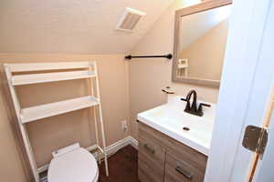 Bathroom with lofted ceiling, toilet, a textured ceiling, vanity, and hardwood / wood-style flooring