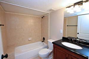 Full bathroom with vanity, a textured ceiling, toilet, and tiled shower / bath