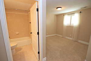 Bathroom with tile patterned floors, a textured ceiling, tiled shower / bath combo, and toilet