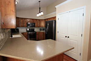 Kitchen with sink, kitchen peninsula, pendant lighting, decorative backsplash, and appliances with stainless steel finishes