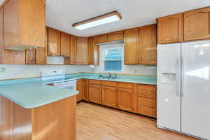 Kitchen featuring sink, light hardwood / wood-style flooring, kitchen peninsula, a textured ceiling, and white appliances