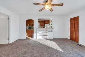 Unfurnished living room featuring carpet floors, ceiling fan, and ornamental molding