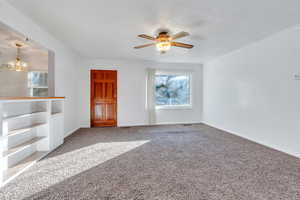 Unfurnished living room featuring ceiling fan with notable chandelier, carpet floors, and crown molding