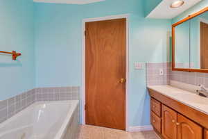 Bathroom featuring tile patterned flooring, vanity, and tiled bath