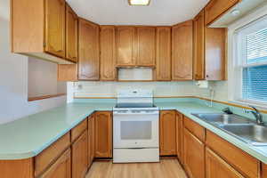 Kitchen featuring backsplash, white range with electric cooktop, sink, and light wood-type flooring