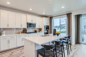 Kitchen with white cabinetry, stainless steel appliances, and a kitchen island with sink