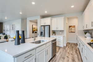 Kitchen with appliances with stainless steel finishes, tasteful backsplash, sink, LVP flooring, and white cabinetry