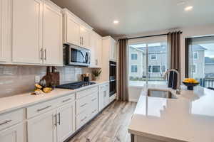 Kitchen featuring a wealth of natural light, sink, backsplash, white cabinets, and appliances with stainless steel finishes