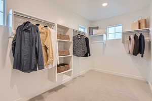 Primary walk in closet with light colored carpet