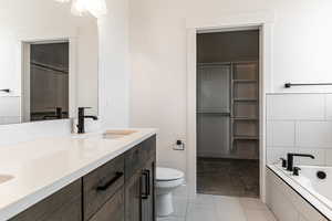 Bathroom with tile patterned flooring, vanity, tiled bath, and toilet