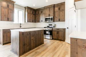 Kitchen with appliances with stainless steel finishes, light wood-type flooring, dark brown cabinets, sink, and a kitchen island