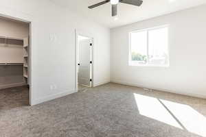 Unfurnished bedroom with carpet, a spacious closet, a closet, and ceiling fan