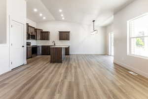 Kitchen featuring appliances with stainless steel finishes, light wood-type flooring, dark brown cabinetry, sink, and pendant lighting