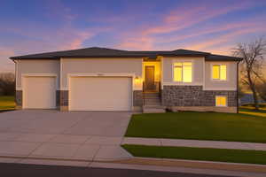 Prairie-style house featuring a garage, concrete driveway, a front yard, and stone siding