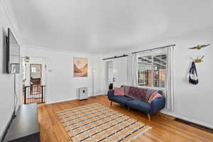 Living room with a barn door, wood-type flooring, and ornamental molding