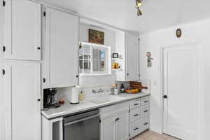 Kitchen with dishwasher, sink, decorative backsplash, light tile patterned floors, and white cabinetry