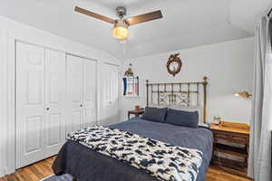 Bedroom featuring multiple closets, ceiling fan, light hardwood / wood-style floors, and vaulted ceiling