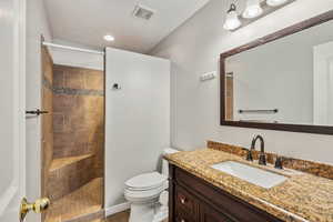 Bathroom featuring tiled shower, a textured ceiling, vanity, and toilet