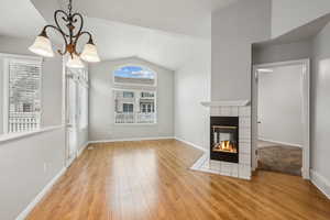 Unfurnished living room featuring a chandelier, light hardwood / wood-style floors, vaulted ceiling, and a fireplace