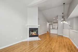 Unfurnished living room featuring a chandelier, light wood-type flooring, a fireplace, and vaulted ceiling