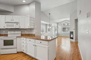 Kitchen with kitchen peninsula, white appliances, white cabinetry, hanging light fixtures, and a tiled fireplace