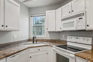 Kitchen featuring white appliances, white cabinetry, dark stone countertops, and sink