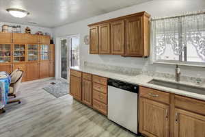 Kitchen featuring dishwasher, light stone counters, sink, and light hardwood / wood-style flooring