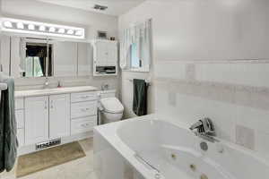 Bathroom with a relaxing tiled tub, toilet, tile walls, and vanity