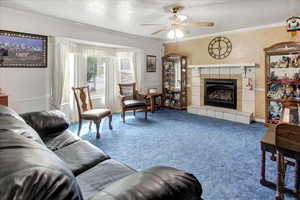 Living room featuring carpet floors, ceiling fan, crown molding, and a tiled fireplace