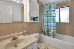 Full bathroom with shower / bathtub combination with curtain, toilet, decorative backsplash, vanity, and tile walls