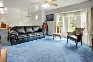 Living room with carpet flooring, ceiling fan with notable chandelier, and ornamental molding