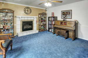 Sitting room featuring carpet flooring, ceiling fan, crown molding, and a tile fireplace