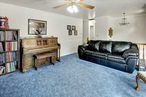 Carpeted living room with ceiling fan with notable chandelier and crown molding