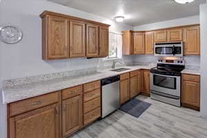 Kitchen featuring light stone countertops, appliances with stainless steel finishes, light wood-type flooring, a textured ceiling, and sink