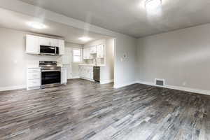 Kitchen with appliances with stainless steel finishes, dark wood-type flooring, and white cabinetry