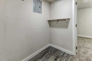 Walk in closet with electric panel and dark wood-type flooring