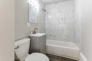 Full bathroom featuring wood-type flooring, vanity, tiled shower / bath combo, and toilet