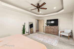 Carpeted bedroom featuring a raised ceiling and ceiling fan