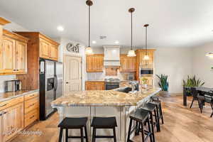 Kitchen featuring custom exhaust hood, sink, appliances with stainless steel finishes, and tasteful backsplash