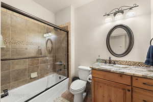 Full bathroom with vanity, backsplash, toilet, and bath / shower combo with glass door