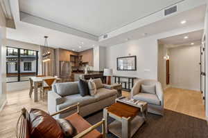 Living room featuring sink, a raised ceiling, a notable chandelier, and light hardwood / wood-style flooring