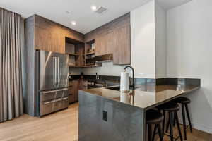 Kitchen featuring a kitchen breakfast bar, light wood-type flooring, kitchen peninsula, high end appliances, and extractor fan