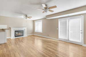 Unfurnished living room with ceiling fan, light wood-type flooring, a tile fireplace, and a textured ceiling