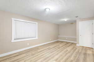 Empty room featuring light wood-type flooring and a textured ceiling