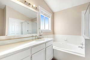 Bathroom with shower with separate bathtub, vanity, and vaulted ceiling