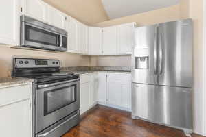 Kitchen with lofted ceiling, white cabinets, dark hardwood / wood-style floors, and appliances with stainless steel finishes