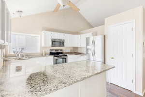 Kitchen featuring appliances with stainless steel finishes, white cabinets, light stone counters, and kitchen peninsula