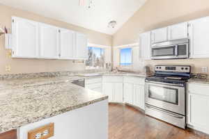 Kitchen with sink, white cabinets, vaulted ceiling, and appliances with stainless steel finishes