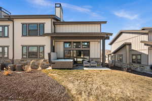 Back of house featuring an outdoor living space, stone siding, a patio area, board and batten siding, and a hot tub