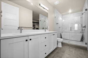 Full bathroom featuring double vanity, a marble finish shower, toilet, and a sink